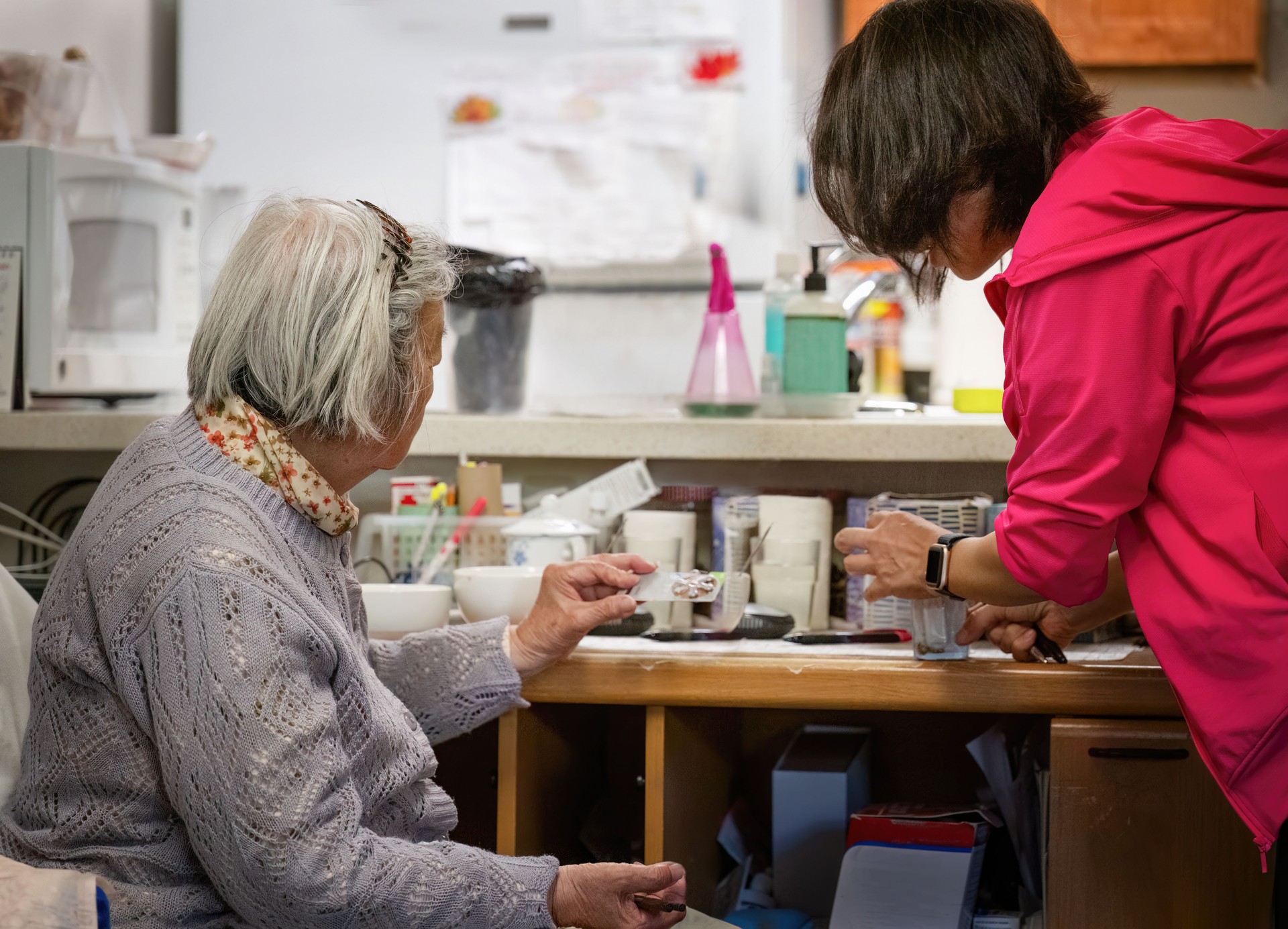 Daughter and senior woman sorting medicine pills at home.